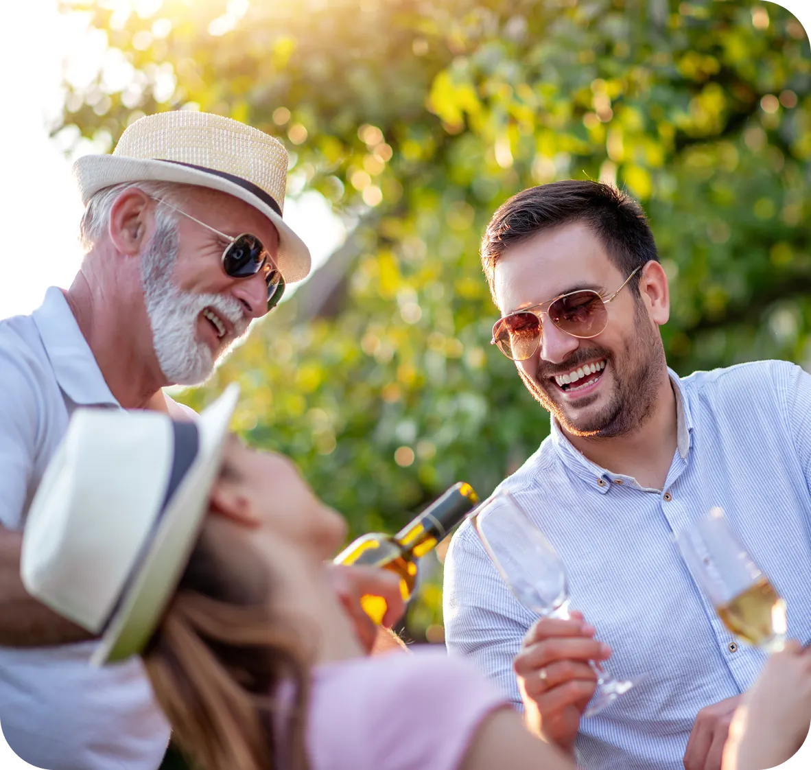 Three adults wearing sunglasses, smiling and enjoying a drink outdoors in sunlight.