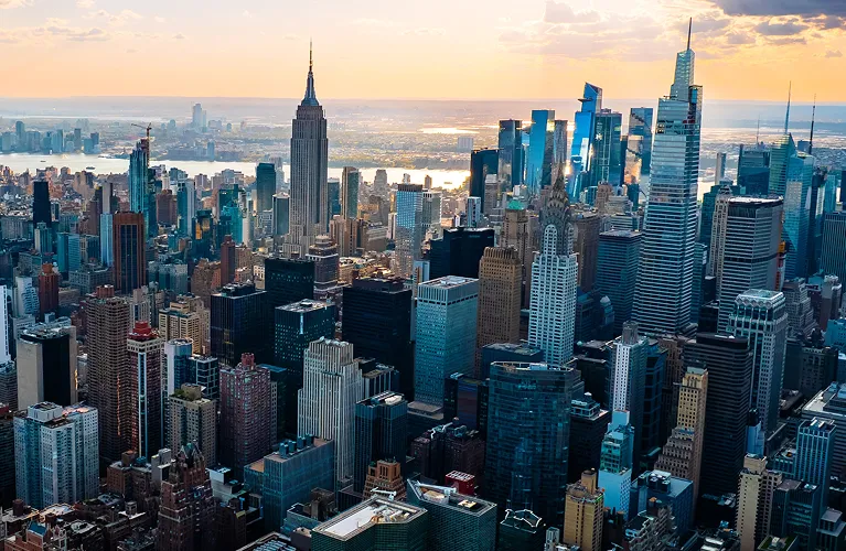 Aerial view of New York City skyline at sunset featuring the Empire State Building and surrounding skyscrapers.