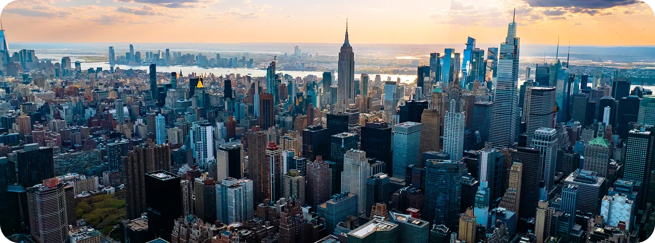 Aerial view of New York City skyline at sunset with prominent skyscrapers and a colorful sky.