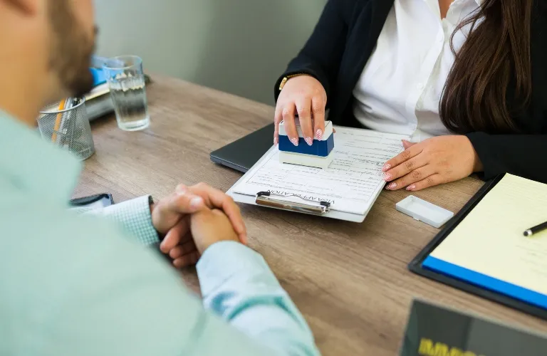 Person stamping a document on a clipboard during a formal office meeting.