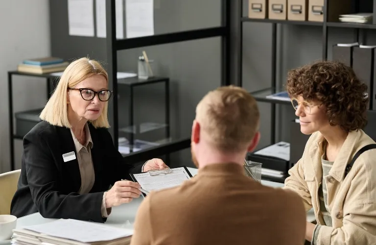 Professional woman with glasses discussing documents with two clients in modern office.