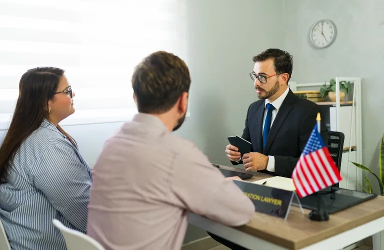 Two clients consulting with a male immigration lawyer in a formal office setting.
