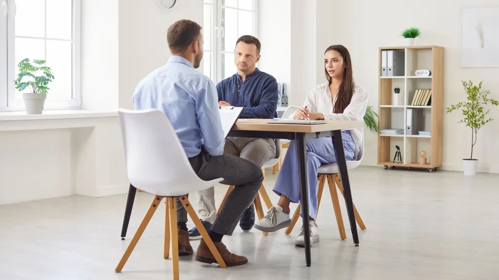 Three professionals engaged in a formal interview in a modern, bright office setting.
