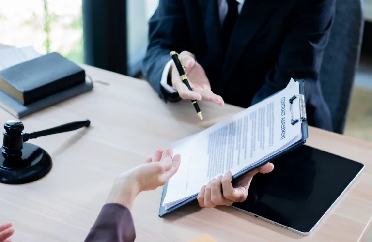 Two business professionals at a desk reviewing a contract agreement on a clipboard.