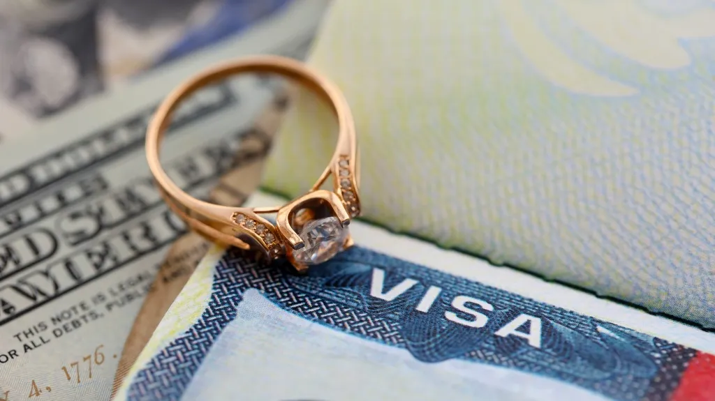 Close-up of a gold ring with diamond placed on a U.S. visa and partially visible dollar bill.