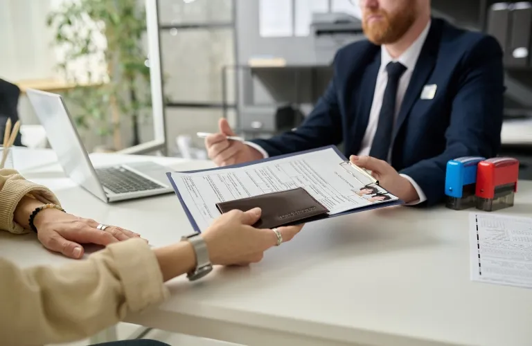 Professional man in suit reviewing documents handed by a person at a white office desk.