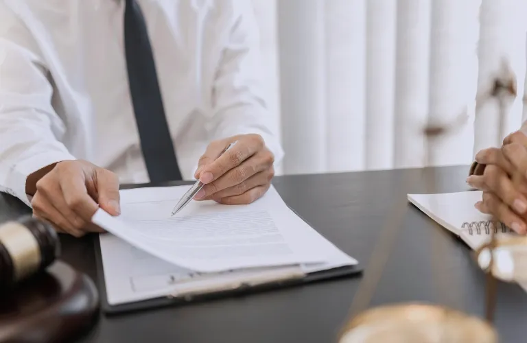 Two individuals at a desk reviewing legal documents, with a gavel and scales of justice visible.